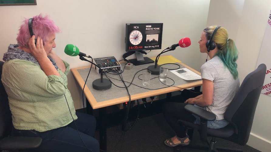 Two women sitting in a radio studio, with microphones and headphones