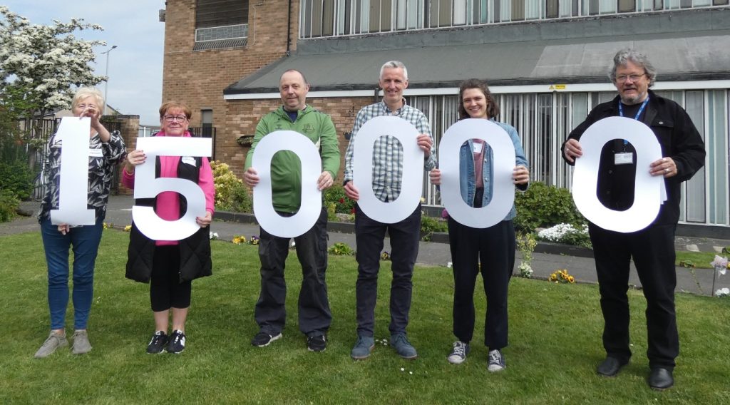 6 people holding cut-out numbers, reading 150,000