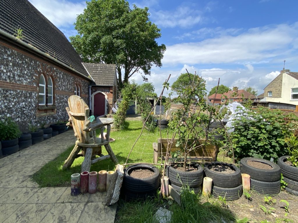 Kirkley Pantry Community Garden: a cultivated area beside the church hall, with tyre planters, benches and a grass area