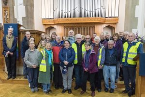 A group of people in front of a church organ. Some are wearing high-vis.