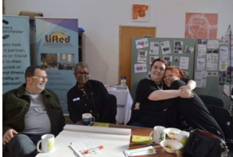 Four people at a table. Two are hugging.