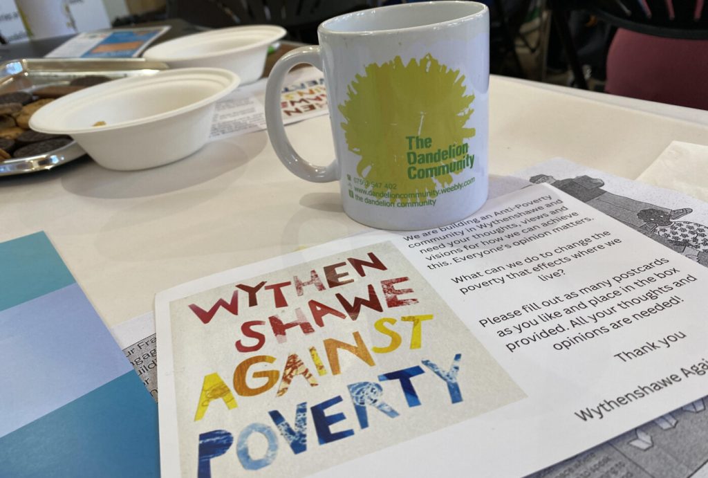A mug with a Dandelion on it, beside a flyer reading Wythenshawe Against Poverty