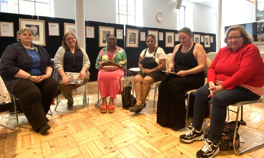 Six people sitting on chairs in a semi-circle, in a church hall