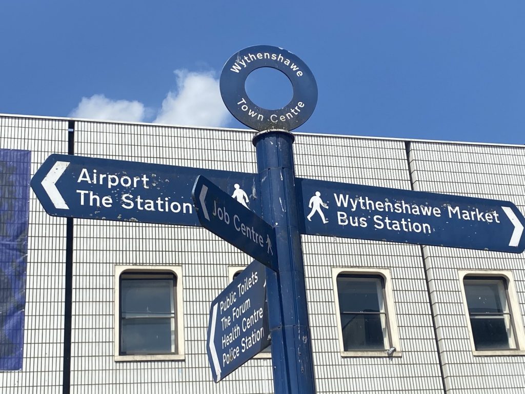 A signpost in Wythensawe, including directions to the airport, station, job centre, bus station, market and health centre