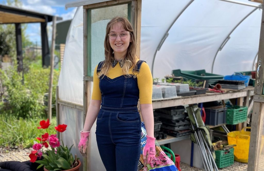 Kerrie Bryan, smiling in front of a polytunnel in the community garden