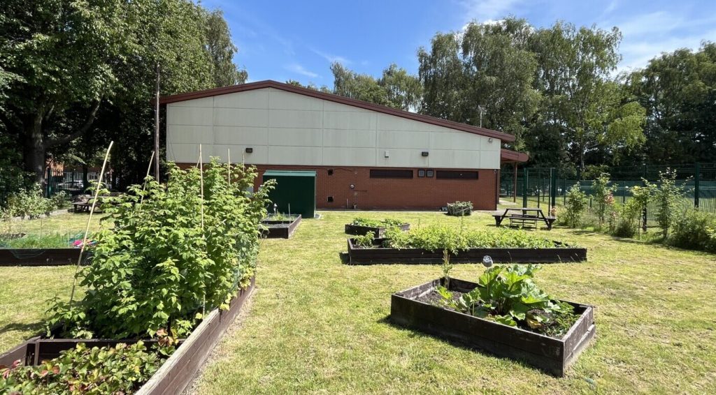 Raised beds in a large garden area, in front of a plain building