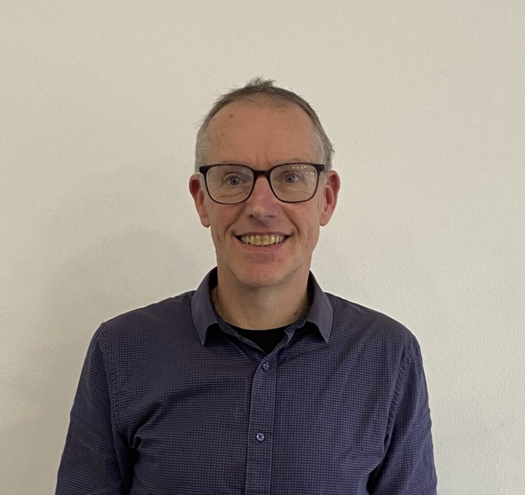 A posed head & shoulders photo of Andy Dickens, director of FCG in Reading. A man in a blue shirt and glasses is smiling to the camera.