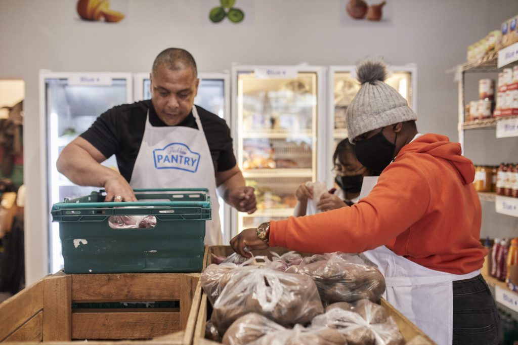 Three people sorting crates of fresh food in a Pantry.