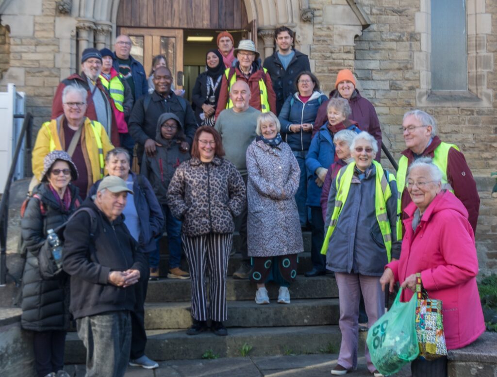 A posed photo of about 20 walkers, standing at a church doorway and steps